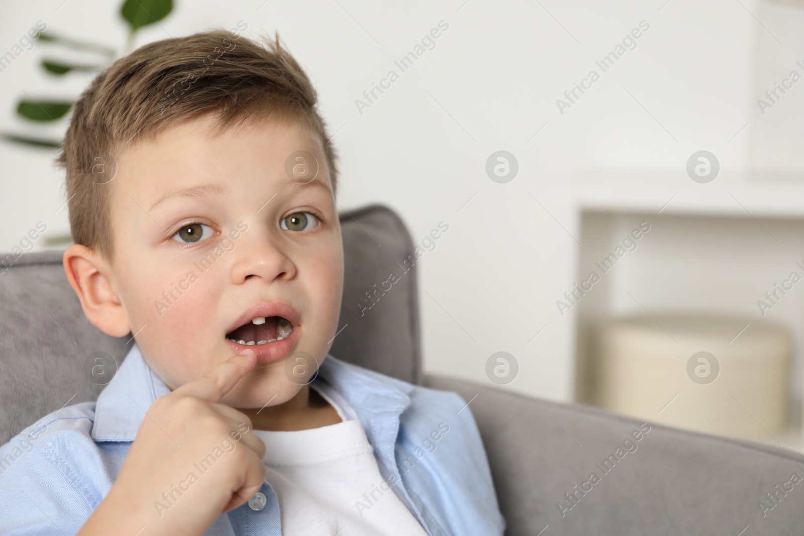 Photo of Cute little boy pointing at his missing tooth indoors