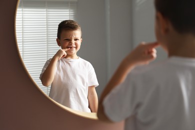 Photo of Cute little boy pointing at his missing tooth near mirror indoors