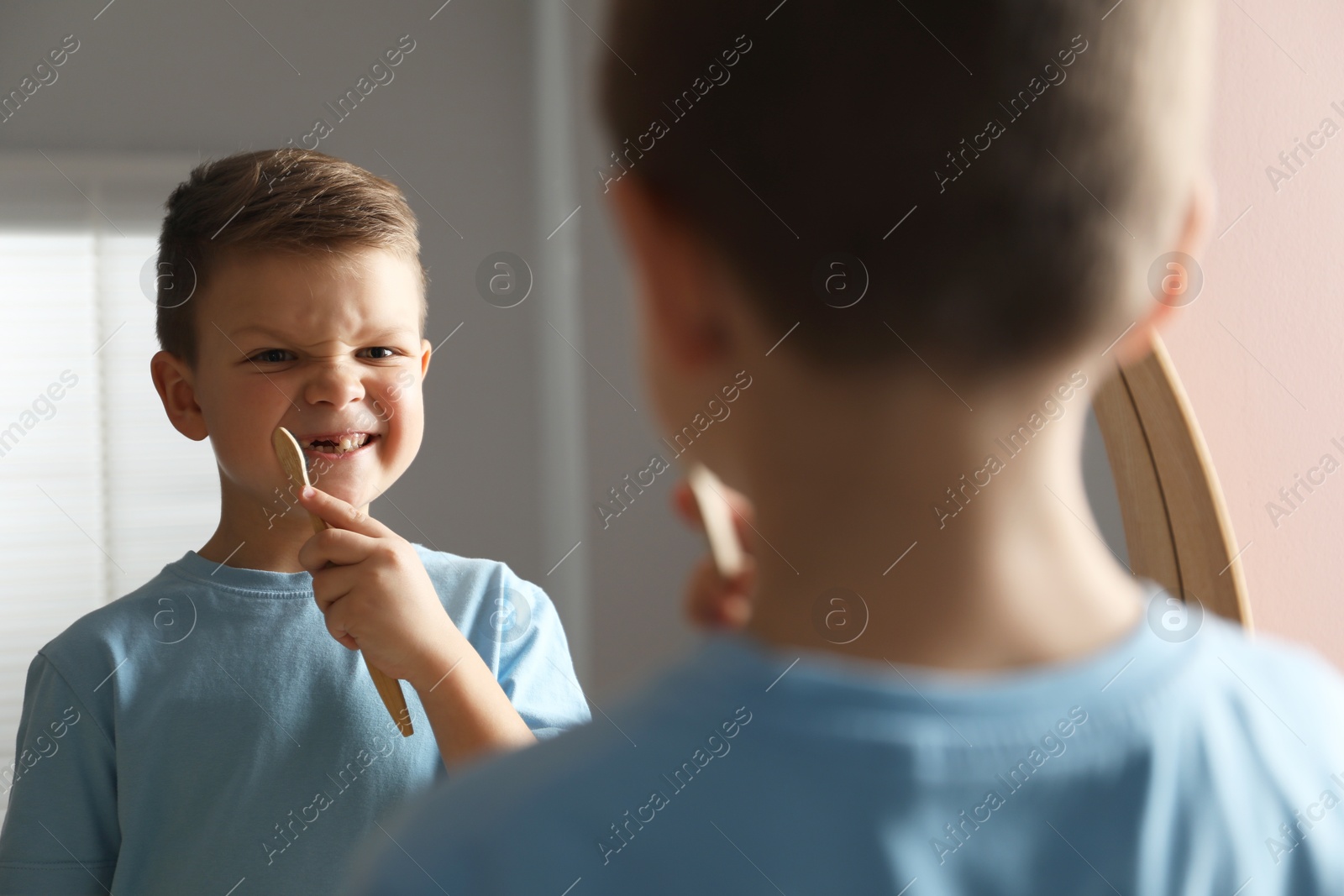 Photo of Cute little boy with missing tooth brushing his teeth near mirror indoors