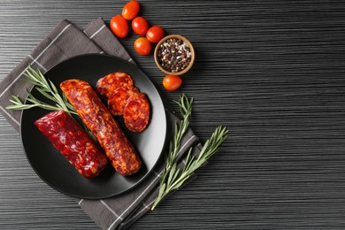 Photo of Cut smoked sausages, rosemary, peppercorns and tomatoes on black wooden table, flat lay. Space for text