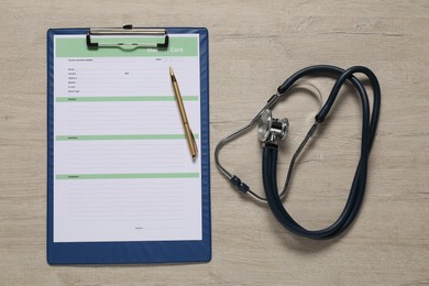 Photo of Medical card form, pen and stethoscope on light wooden background, top view