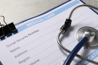 Medical card form and stethoscope on grey background, closeup