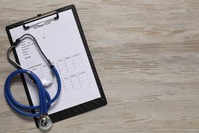 Photo of Medical card form and stethoscope on light wooden background, top view. Space for text