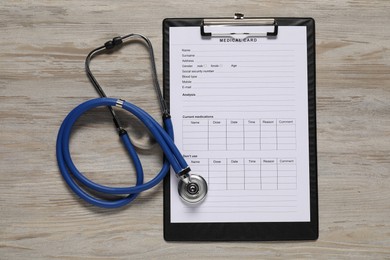 Medical card form and stethoscope on light wooden background, top view