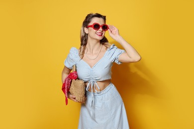 Photo of Happy pin-up woman in sunglasses posing with bag on orange background