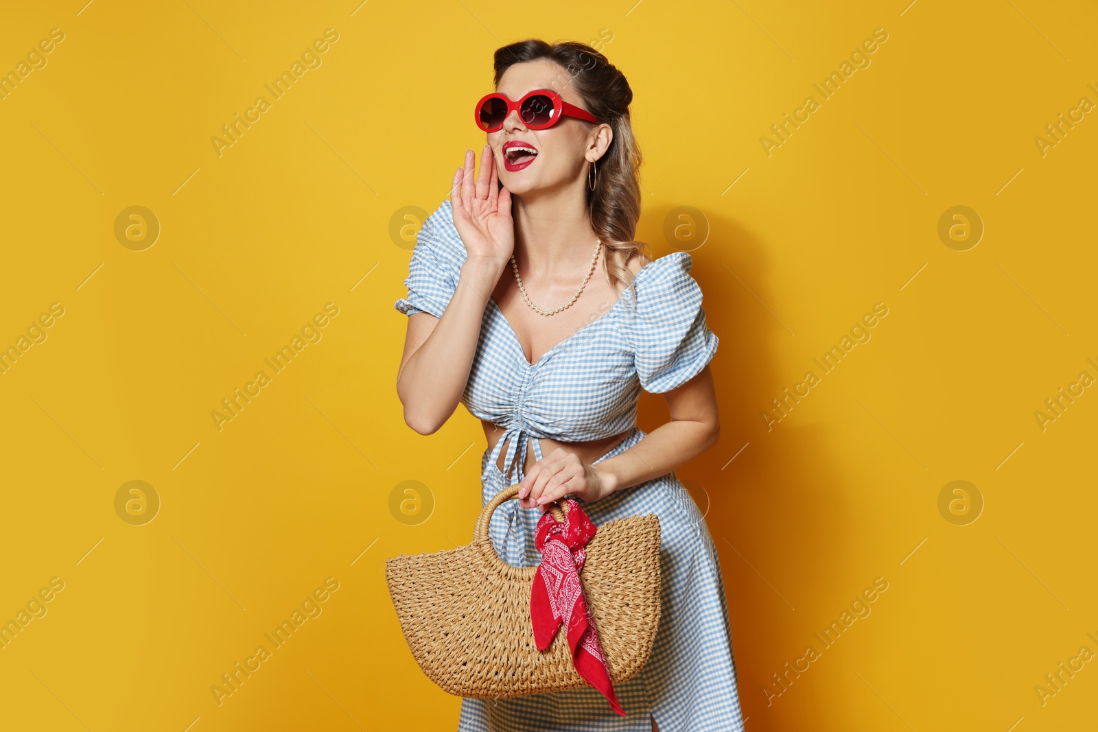 Photo of Beautiful pin-up woman in sunglasses posing with bag on orange background