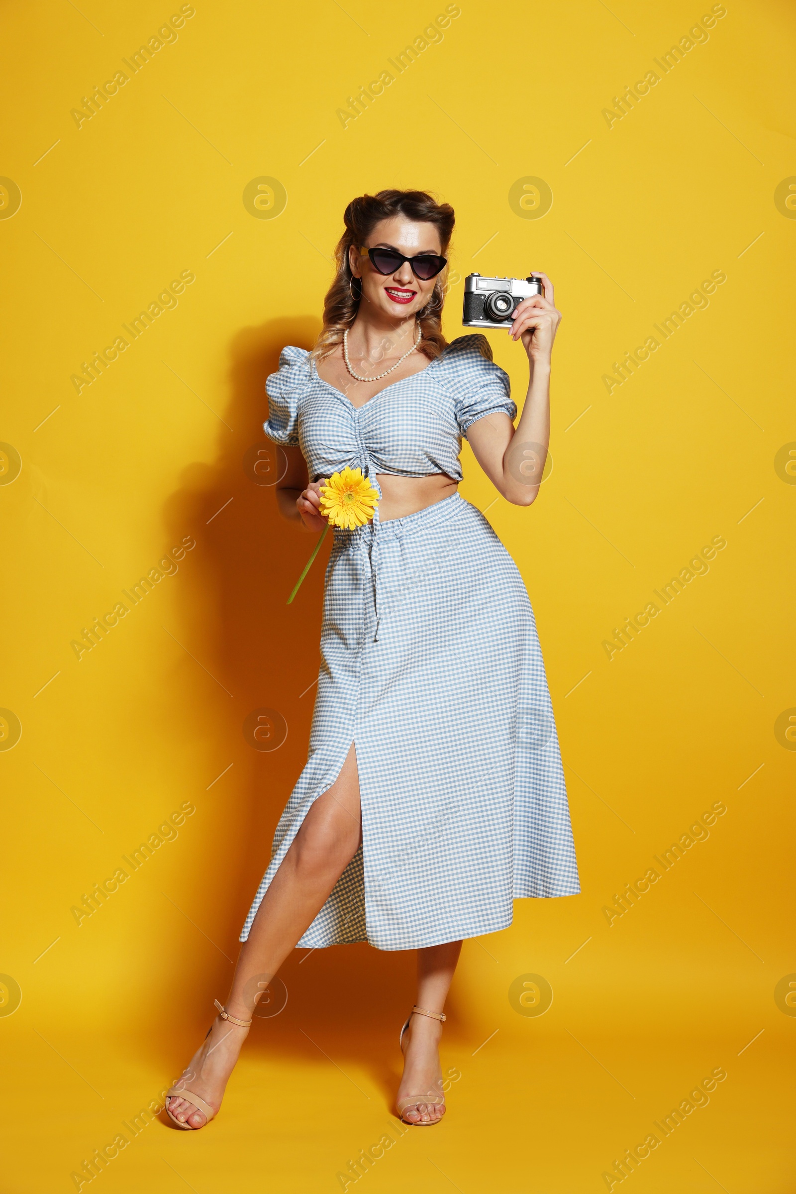 Photo of Happy pin-up woman with camera and flower on orange background