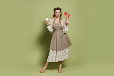 Photo of Happy woman with cupcake and cooking utensils on green background. Pin-up vibes