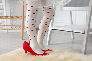 Photo of Little girl wearing oversized high heeled shoes indoors, closeup