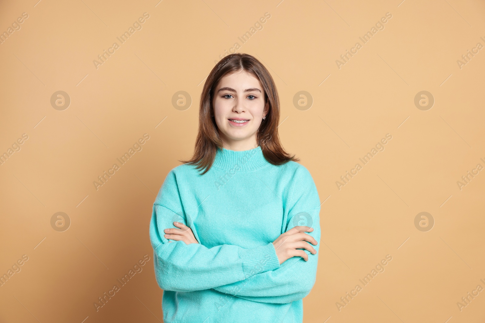 Photo of Portrait of beautiful teenage girl with crossed arms on beige background