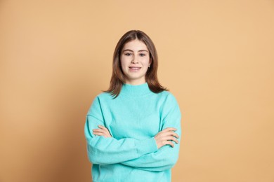 Photo of Portrait of beautiful teenage girl with crossed arms on beige background