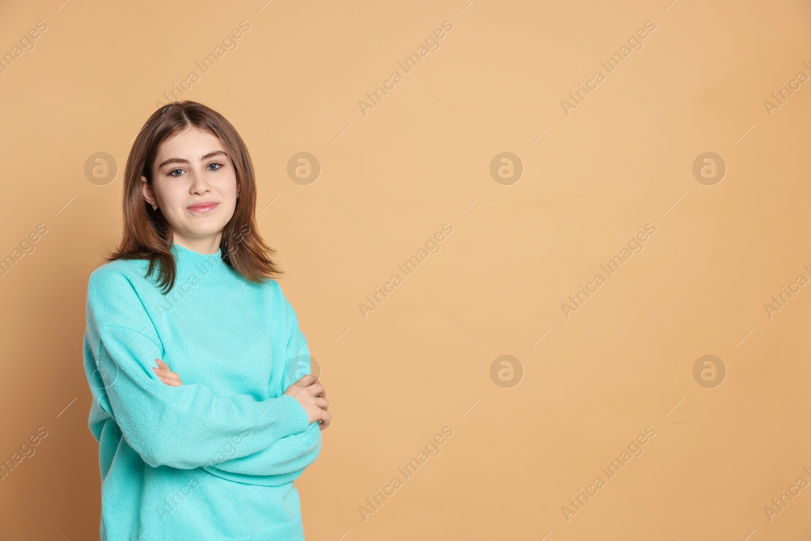 Photo of Portrait of beautiful teenage girl with crossed arms on beige background. Space for text