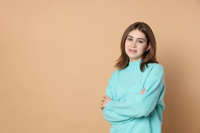 Photo of Portrait of beautiful teenage girl with crossed arms on beige background. Space for text