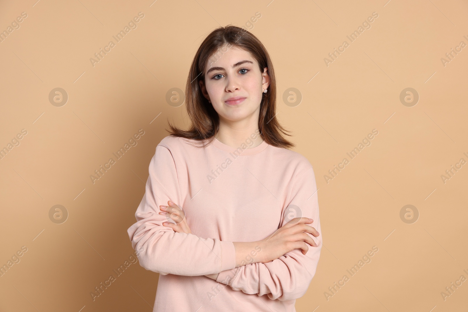 Photo of Portrait of beautiful teenage girl with crossed arms on beige background