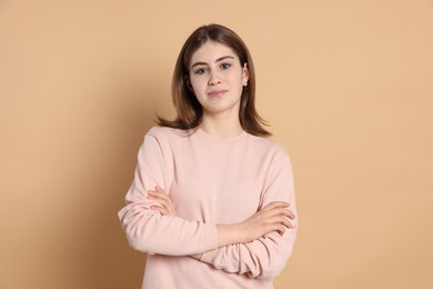 Photo of Portrait of beautiful teenage girl with crossed arms on beige background