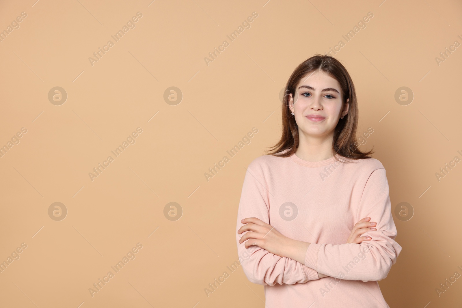 Photo of Portrait of beautiful teenage girl with crossed arms on beige background. Space for text