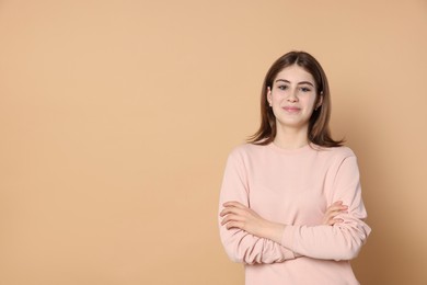 Photo of Portrait of beautiful teenage girl with crossed arms on beige background. Space for text