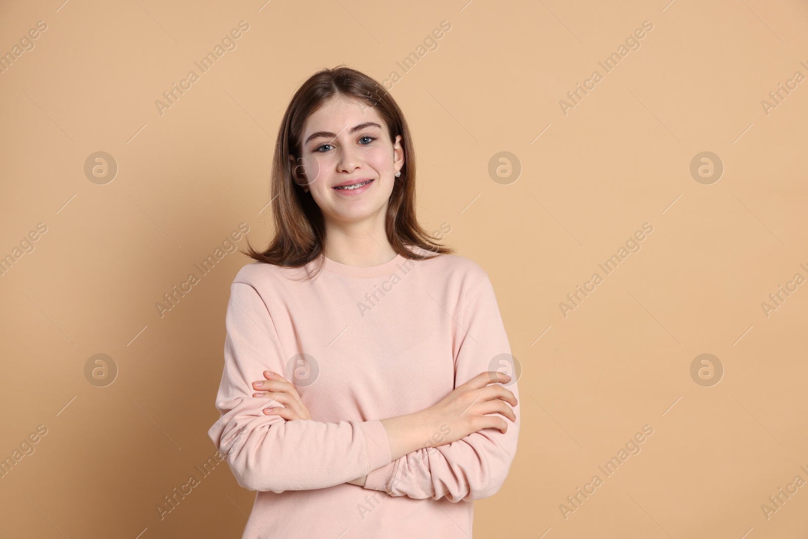 Photo of Portrait of beautiful teenage girl with crossed arms on beige background. Space for text