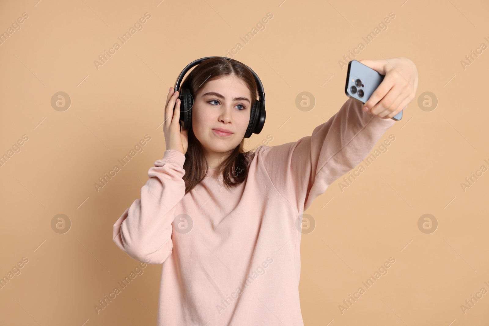 Photo of Portrait of teenage girl in headphones taking selfie on beige background