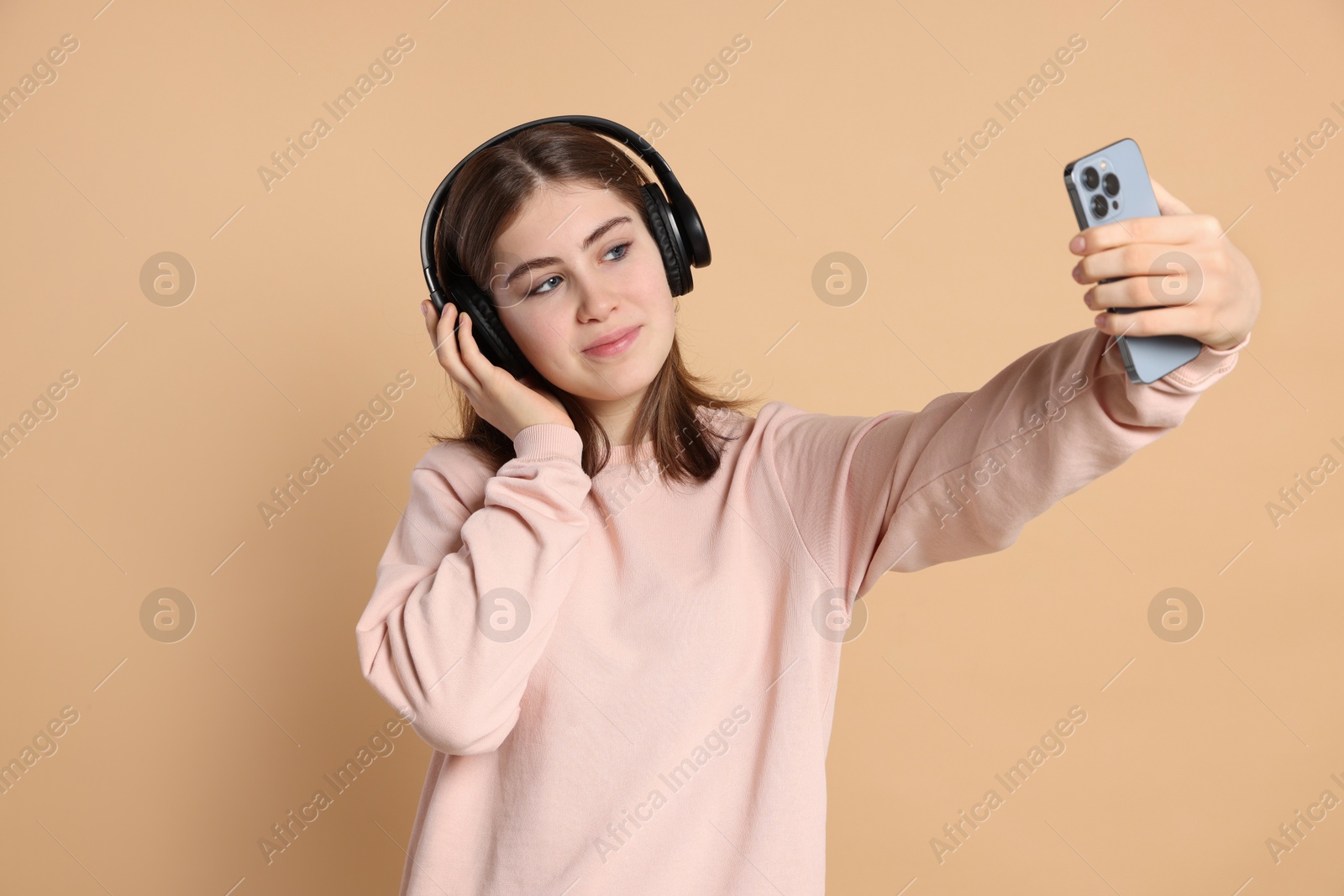 Photo of Portrait of teenage girl in headphones taking selfie on beige background