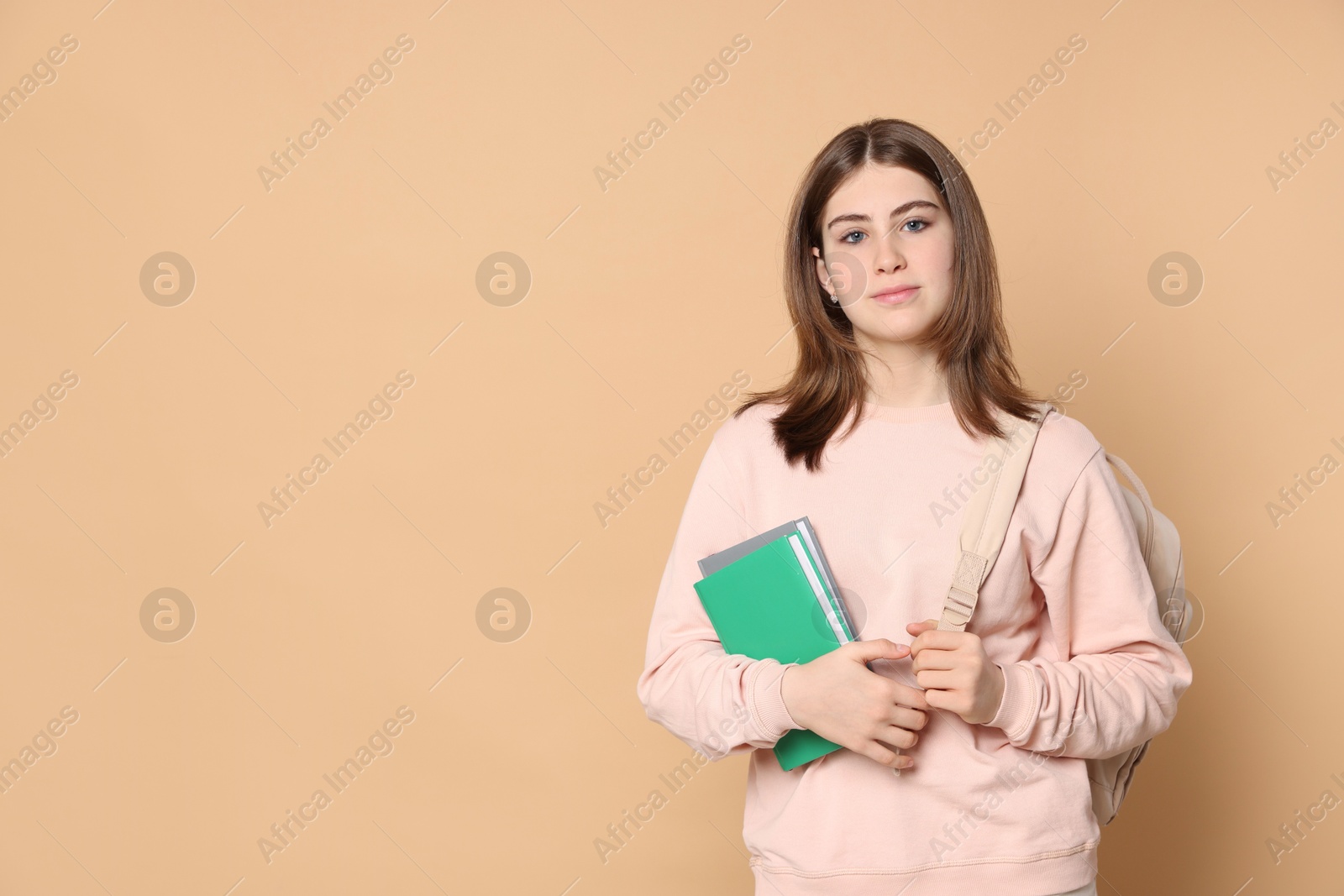 Photo of Portrait of teenage girl with books and backpack on beige background. Space for text