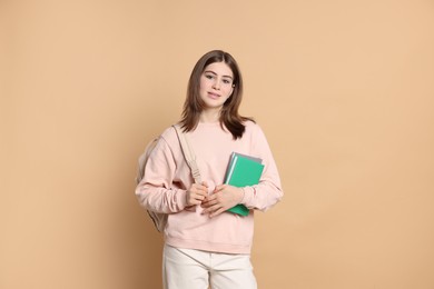 Photo of Portrait of teenage girl with books and backpack on beige background