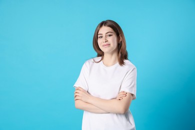 Photo of Portrait of beautiful teenage girl with crossed arms on light blue background. Space for text