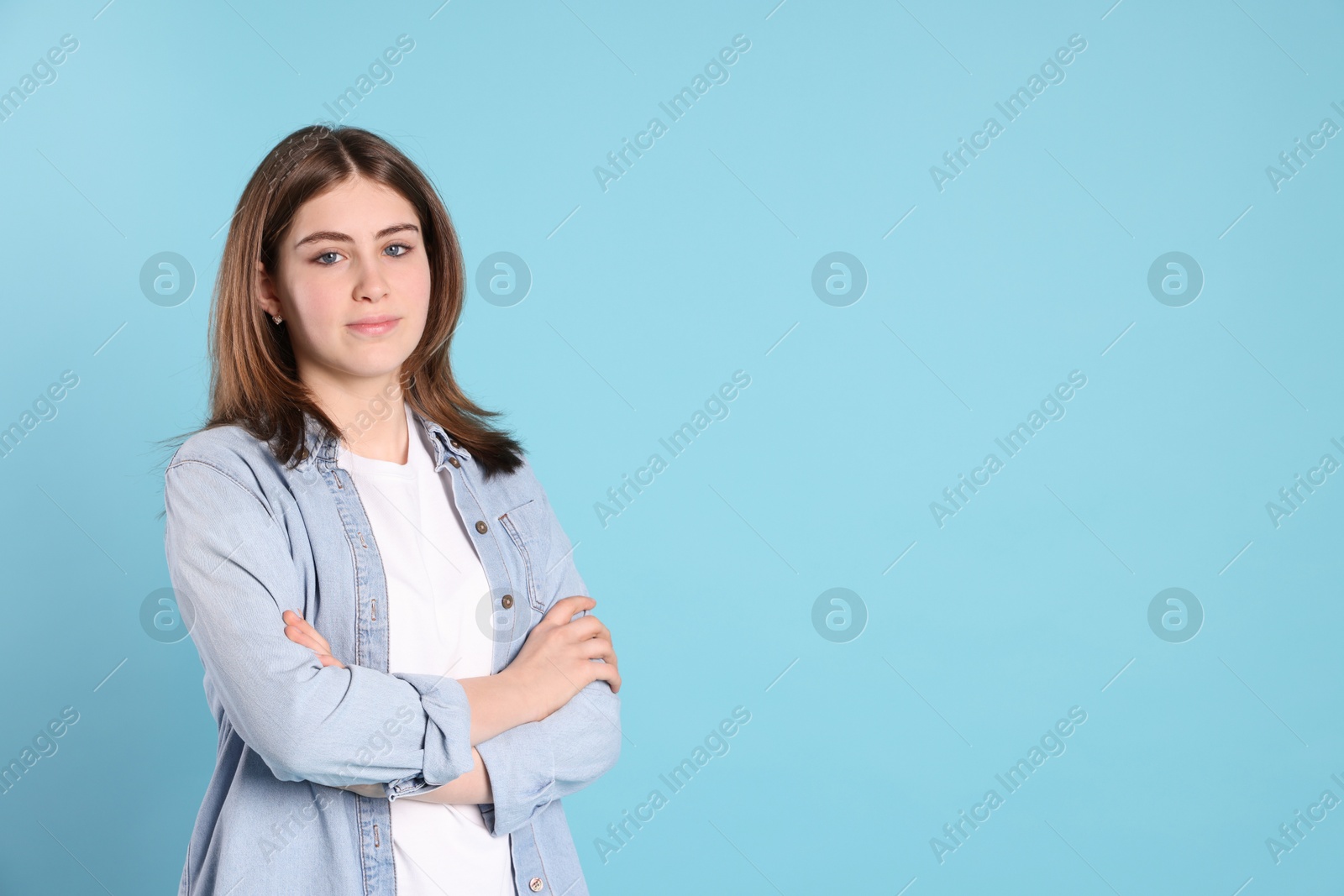 Photo of Portrait of beautiful teenage girl with crossed arms on light blue background. Space for text