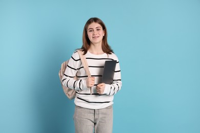 Photo of Portrait of teenage girl with laptop and backpack on light blue background