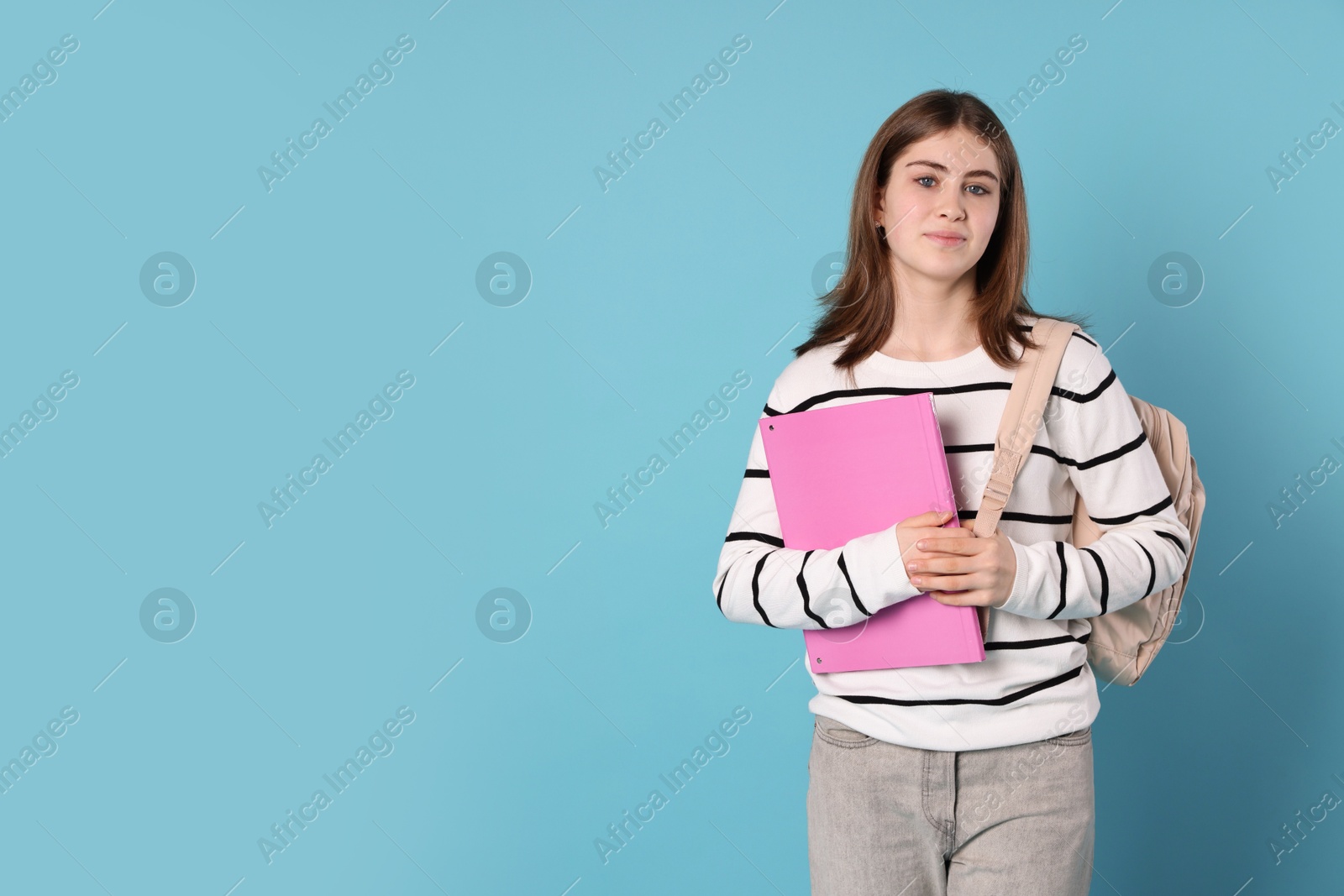 Photo of Portrait of teenage girl with backpack and folder on light blue background. Space for text