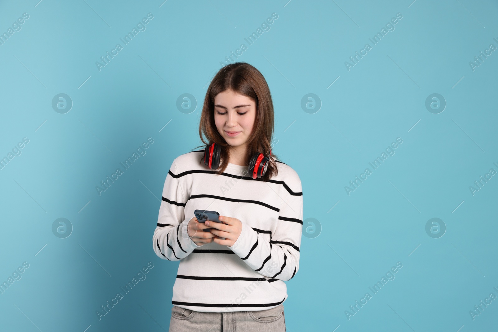 Photo of Portrait of teenage girl with headphones using smartphone on light blue background