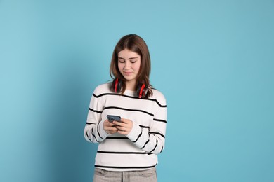 Photo of Portrait of teenage girl with headphones using smartphone on light blue background