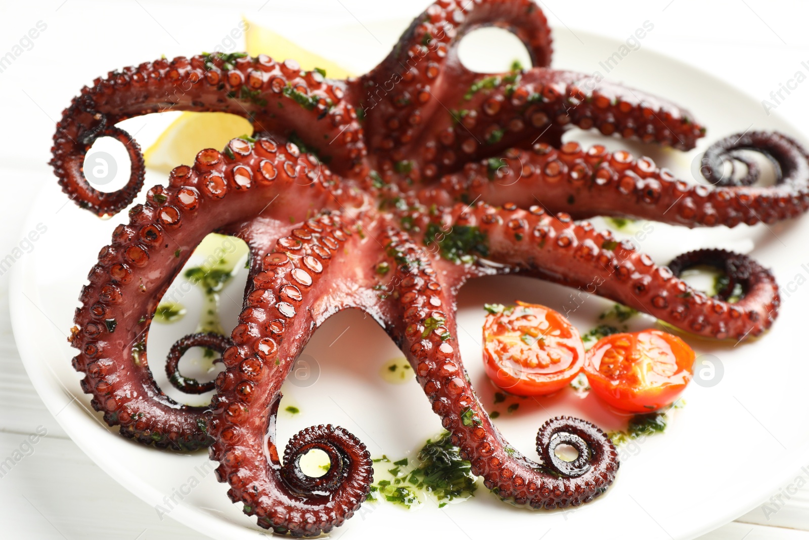 Fried octopus with herb sauce and tomatoes on white wooden table, closeup Photo of Fried octopus with herb sauce and tomatoes on white wooden table, closeup