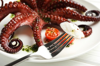 Photo of Eating tasty fried octopus with herb sauce at white wooden table, closeup