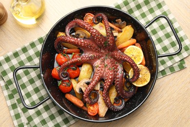 Fried octopus with mushrooms, lemon and vegetables in pan on wooden table, top view