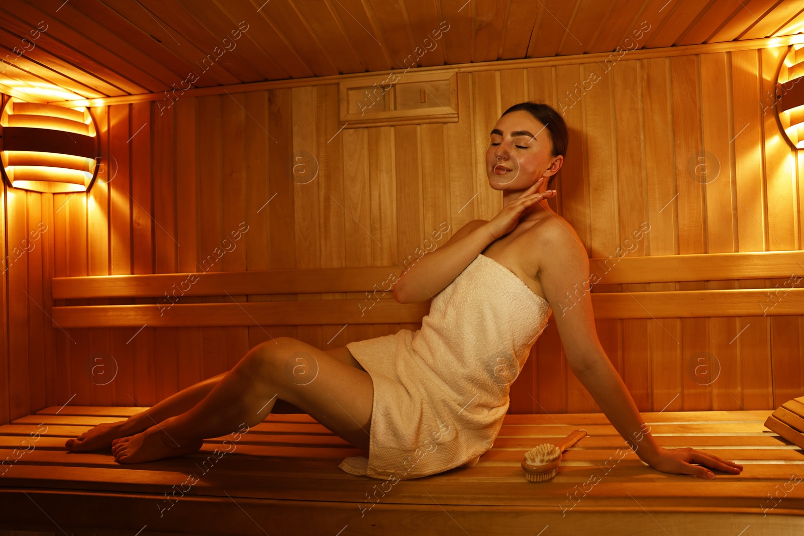 Photo of Beautiful woman wrapped in towel on bench at sauna