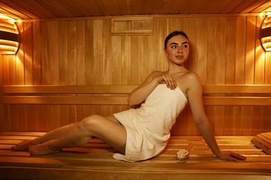 Photo of Beautiful woman wrapped in towel on bench at sauna