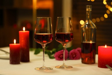 Photo of Romantic place setting with red wine and burning candles on table