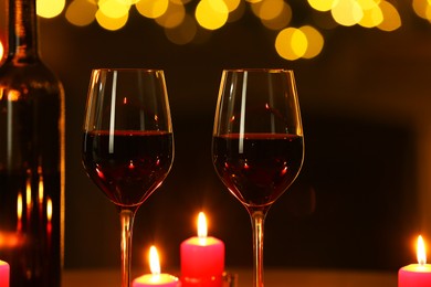 Photo of Glasses of red wine and burning candles against blurred lights, closeup. Romantic dinner