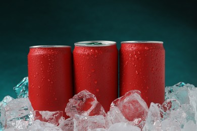 Photo of Refreshing drinks in cans on ice cubes against teal background, closeup