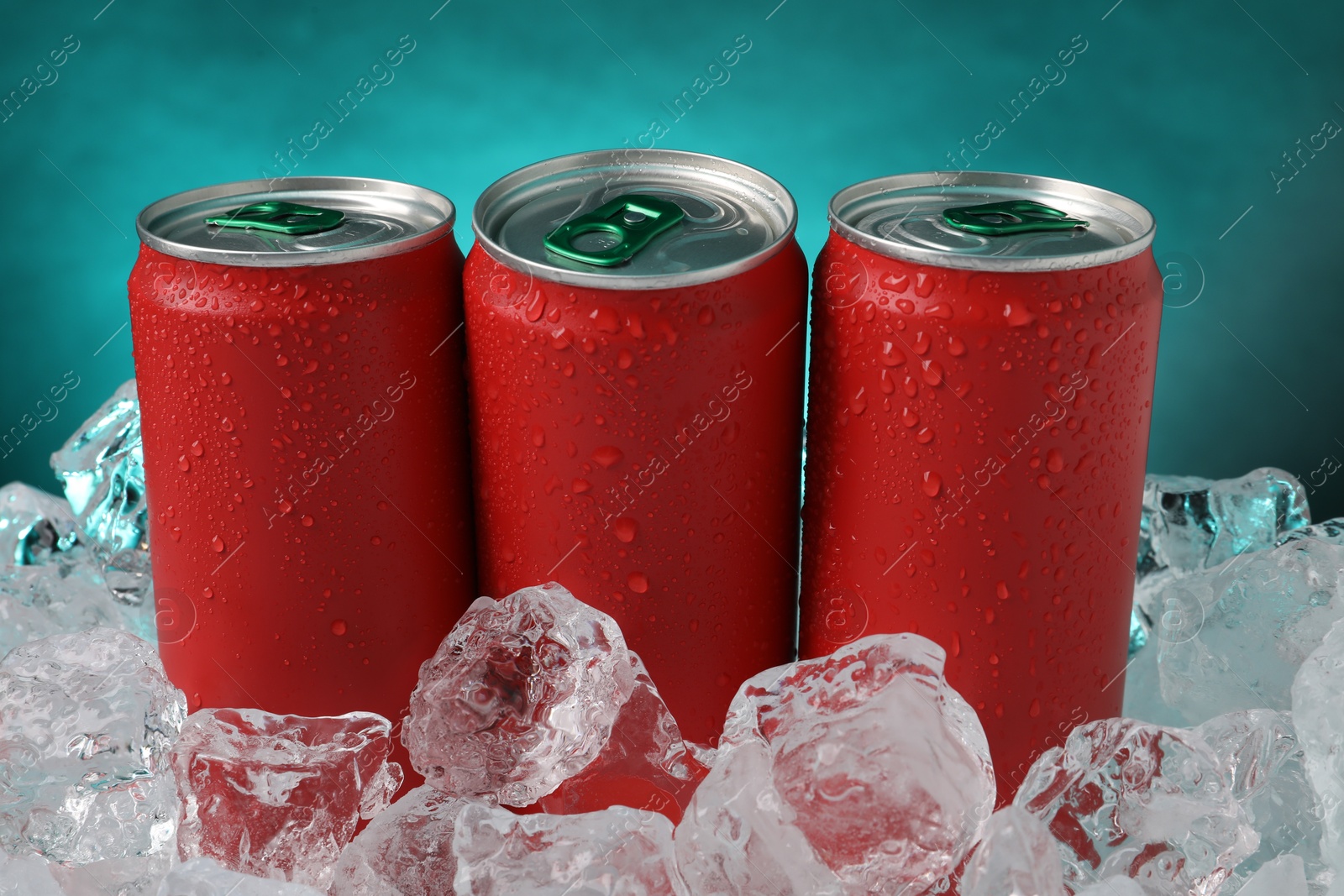 Refreshing drinks in cans on ice cubes against teal background, closeup Photo of Refreshing drinks in cans on ice cubes against teal background, closeup