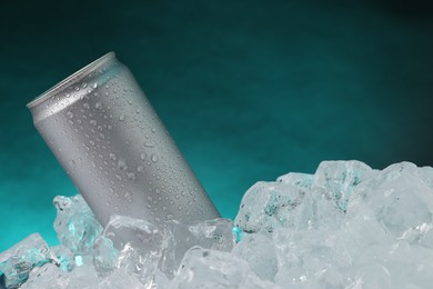 Photo of Refreshing drink in can on ice cubes against teal background, closeup