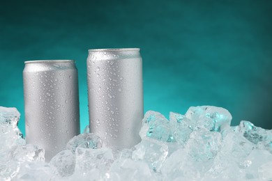 Photo of Refreshing drinks in cans on ice cubes against teal background, closeup