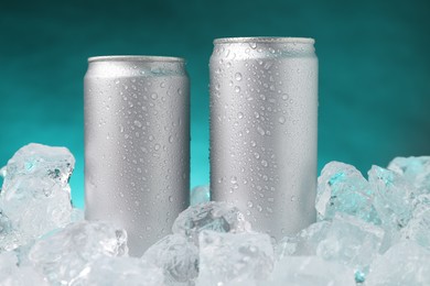 Photo of Refreshing drinks in cans on ice cubes against teal background, closeup