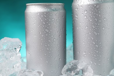 Photo of Refreshing drinks in cans on ice cubes against teal background, closeup