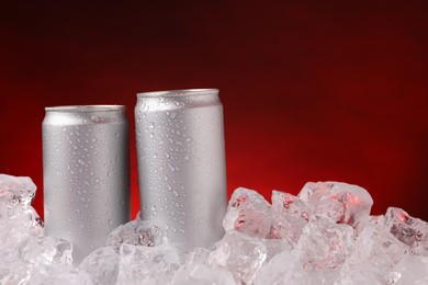 Photo of Refreshing drinks in cans on ice cubes against dark red background, closeup