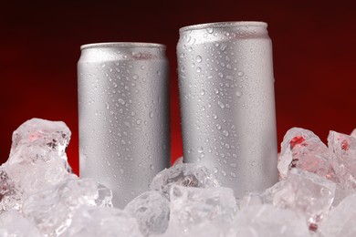 Photo of Refreshing drinks in cans on ice cubes against dark red background, closeup