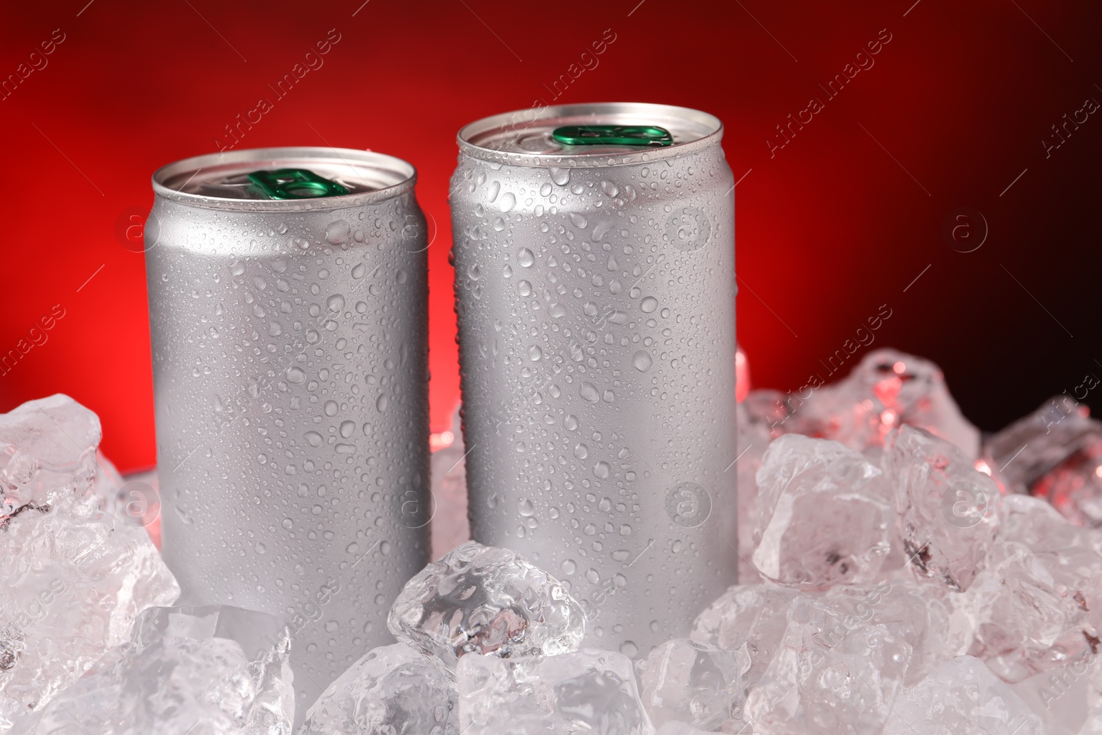 Refreshing drinks in cans on ice cubes against dark red background, closeup Photo of Refreshing drinks in cans on ice cubes against dark red background, closeup