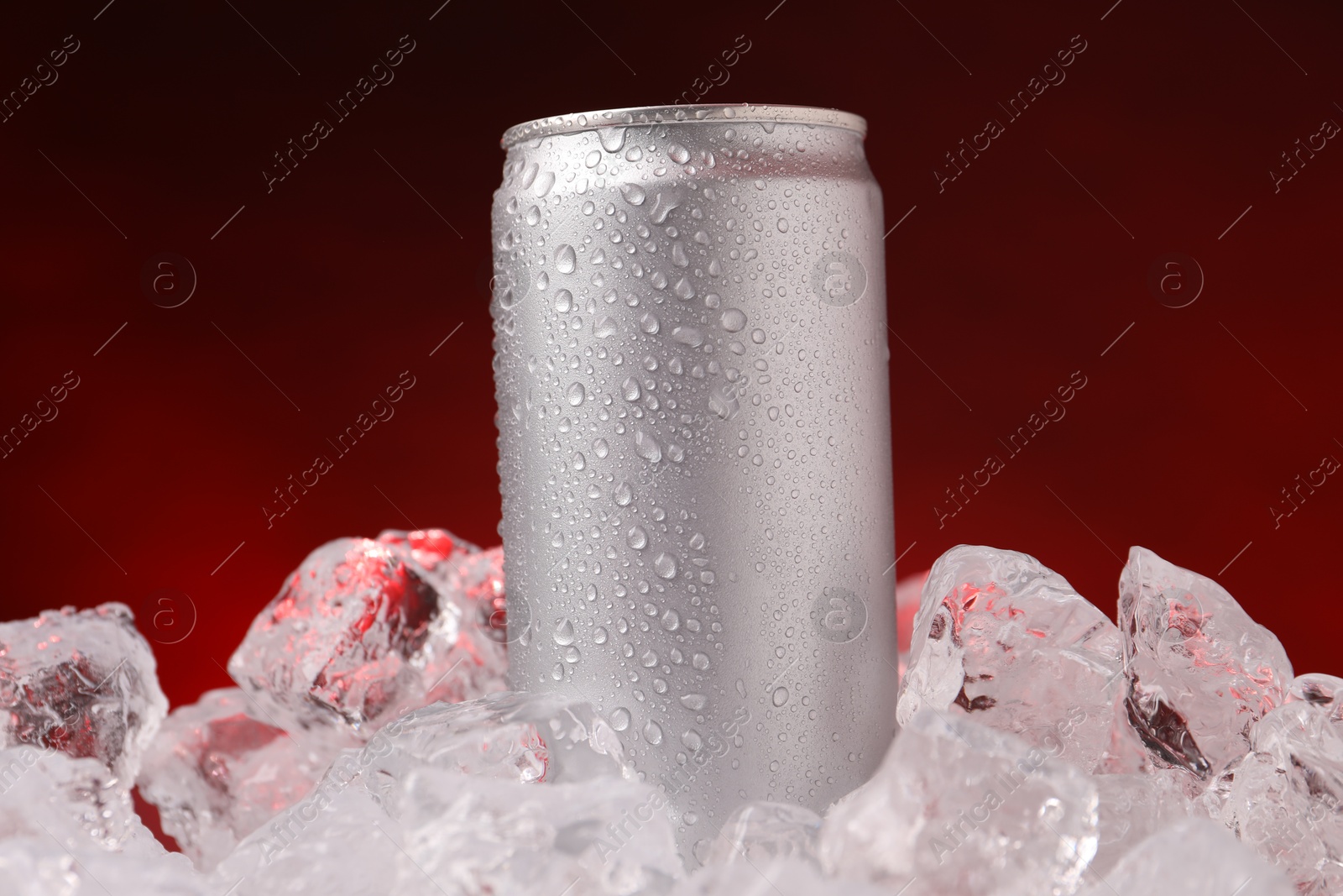 Refreshing drink in can on ice cubes against dark red background, closeup Photo of Refreshing drink in can on ice cubes against dark red background, closeup