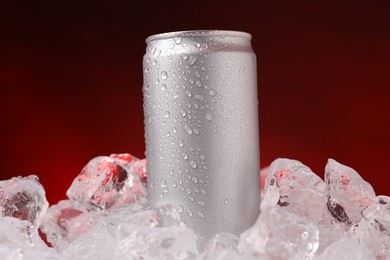 Photo of Refreshing drink in can on ice cubes against dark red background, closeup